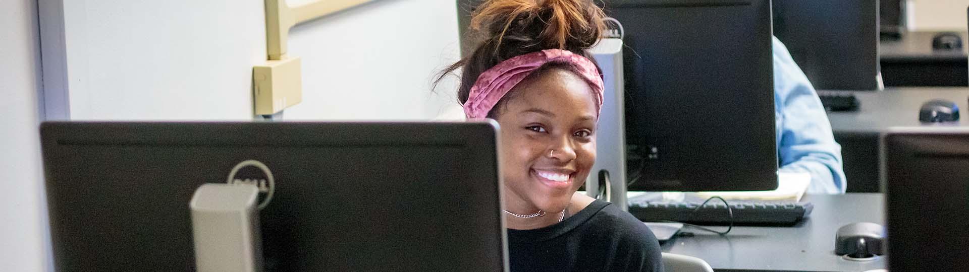 Tulane SoPA student sitting at a computer station and smiling at the camera