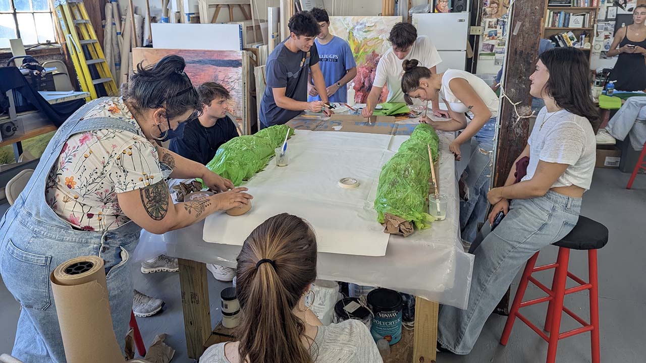 Art students working on a large collaborative project on a table.