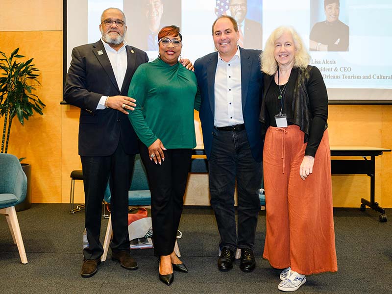 Four people pose for a photo in front of a presentation screen.