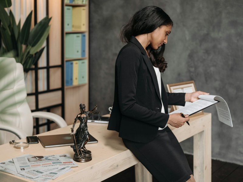 Woman in a black suit reviews documents at a desk.