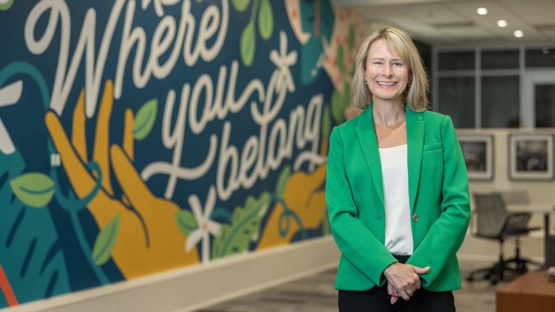 Amelia Manning smiles in front of a mural that says "Where you belong."