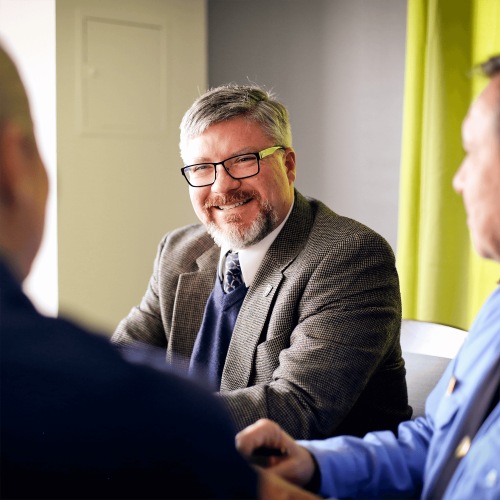 Smiling man in glasses and tweed jacket at a meeting at Tulane School of Professional Advancement, New Orleans Uptown Campus.