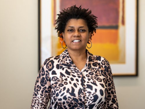 A woman with dark, curly hair smiles, wearing a leopard-print shirt and hoop earrings.
