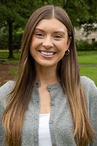 Woman with long brown hair smiling, wearing a gray cardigan.