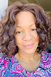 Photograph of a woman with curly brown hair and a colorful patterned top.