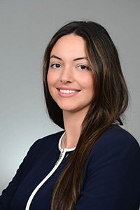 A smiling woman with long, dark hair wears a dark blue jacket.