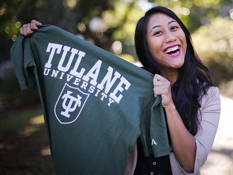 Tulane student holding up Tulane University t-shirt and smiling - Tulane SoPA