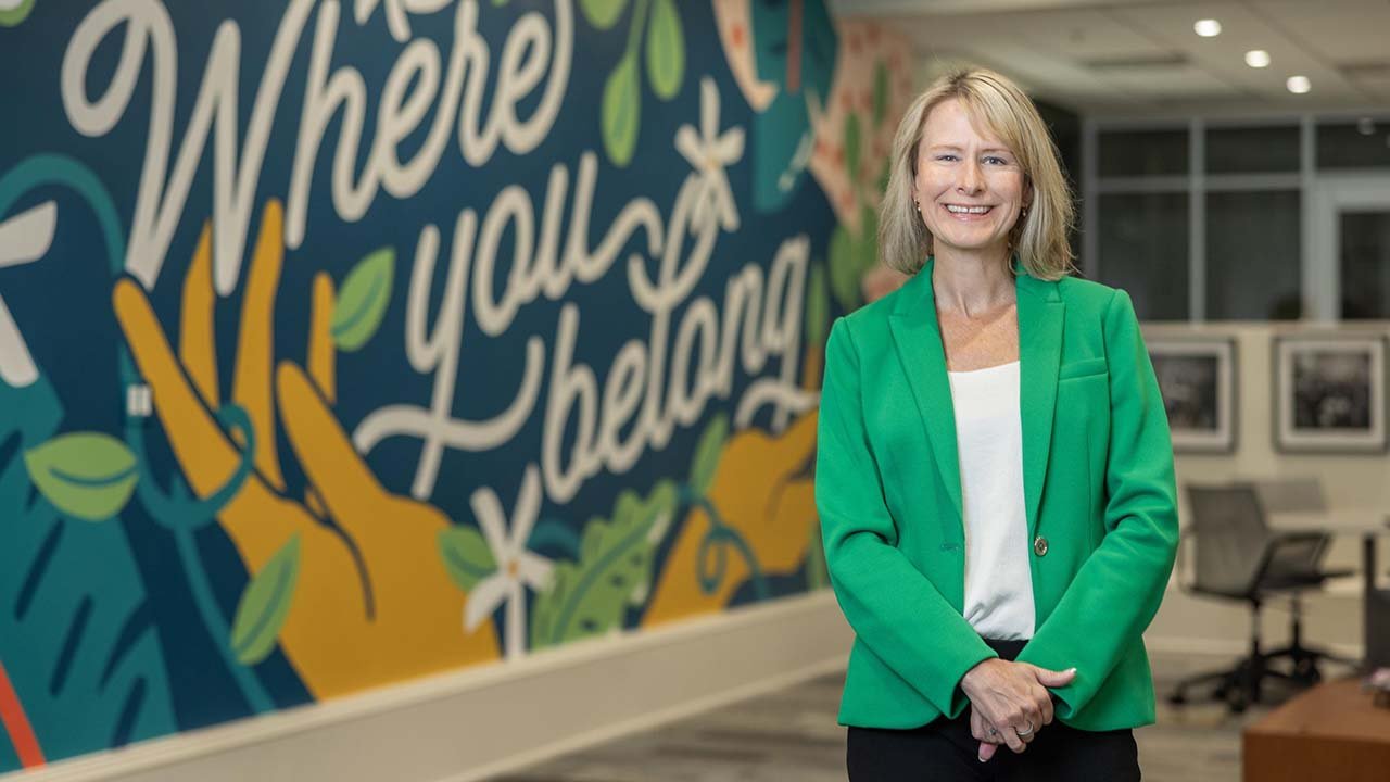 Amelia Manning smiles in front of a mural that says "Where you belong."