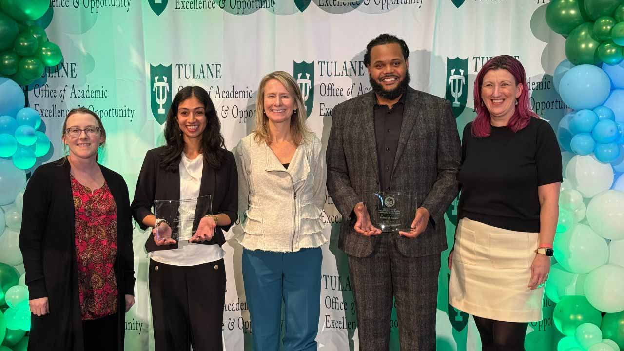 Five people, three women and two men, stand with awards in front of a Tulane University backdrop.