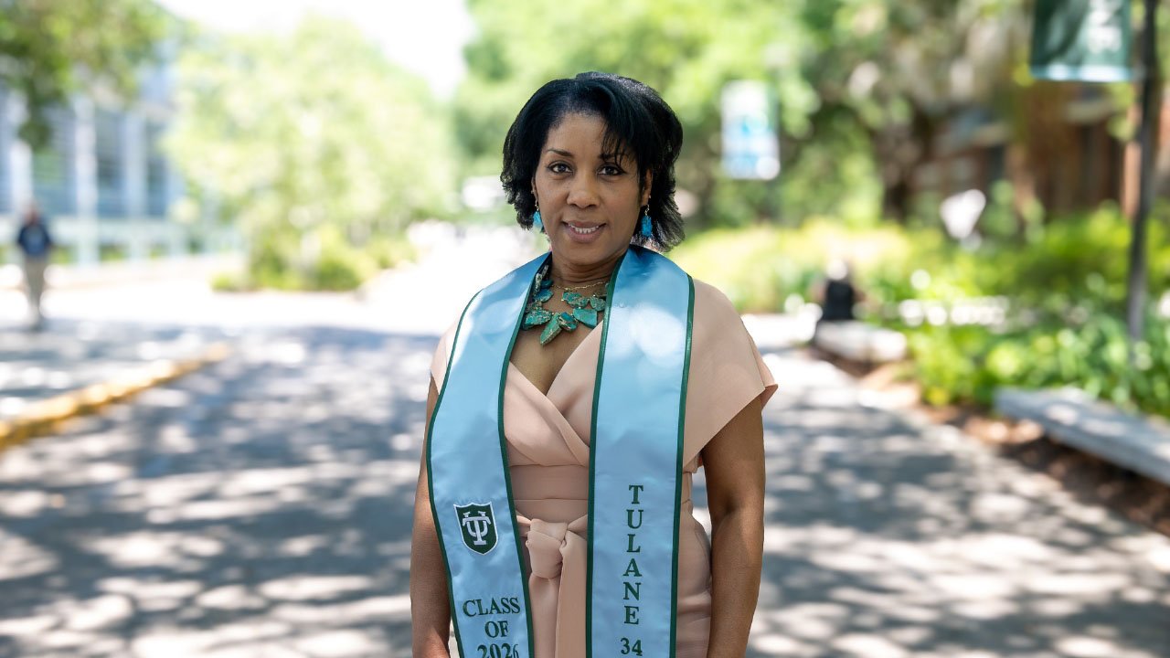 A woman smiles, wearing a light peach dress and a light blue graduation stole that says "Tulane" and "Class of 2022."