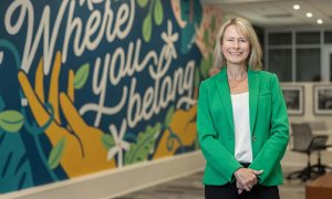 Amelia Manning smiles in front of a mural that says "Where you belong."
