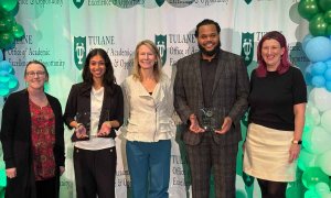 Five people, three women and two men, stand with awards in front of a Tulane University backdrop.