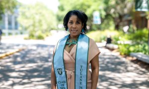 A woman smiles, wearing a light peach dress and a light blue graduation stole that says "Tulane" and "Class of 2022."