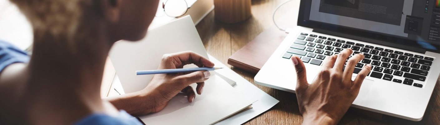 A person typing on their laptop and taking notes