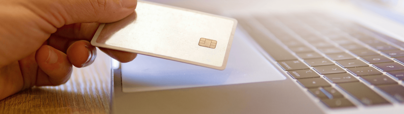 A person holding their credit card by their computer