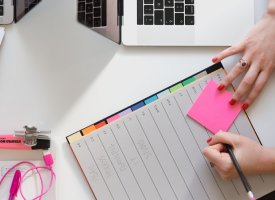 A person writing on a sticky note in their planner