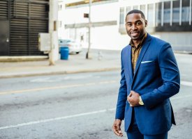 Smiling Black man in a blue suit stands on a city street.