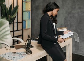 Woman in a black suit reviews documents at a desk.